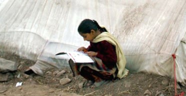 A Pakistani Kashmiri girl studies her schoolbooks outside a tent in a relief camp at Ghari Dupatta