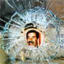 A portrait of Saddam Hussein lies behind a bullet hole in a shop window in Baghdad