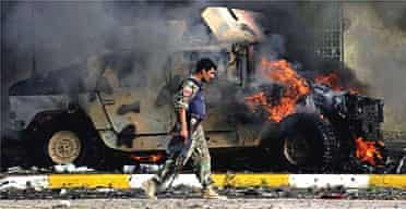 An Iraqi police commando walks by a burning humvee at the site of a suicide car bombing in the northern Iraqi oil hub of Kirkuk