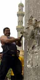 Kadhim al-Jubouri swings a hammer at the base of a statue of Saddam Hussein