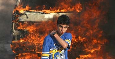 A young Palestinian in front of a burning vehicle in Gaza