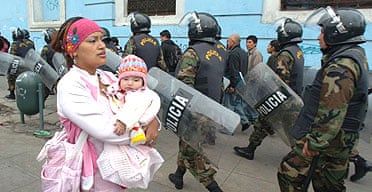 A Peruvian woman carries her child past a riot police patrol in central Lima