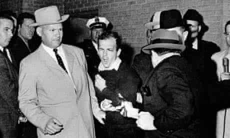 Lee Harvey Oswald, accused assassin of US president John F. Kennedy, reacts as Dallas night club owner Jack Ruby, foreground, shoots at him from point blank range in a corridor of Dallas police headquarters in 1963. The plainclothesman at left is Jim A. Leavelle
