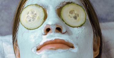 A woman recieving a spa treatment with a blue facial mask and cucumber slices on her eyes