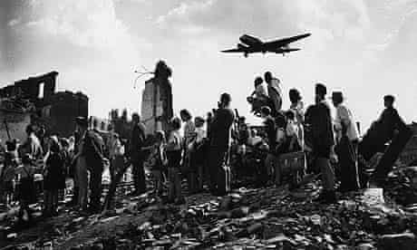Citizens of Berlin stand amid rubble at the edge of Tempelhof airfield to watch an American C-47 cargo plane arrive with food & supplies in July 1948