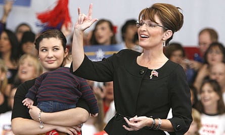 Sarah Palin, with her daughter Willow, holding her brother Trig, campaigns at a rally in Henderson, Nevada. Palin is giving the American sign language hand sign for "I Love You".
