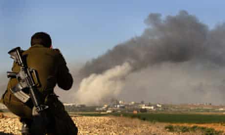 An Israeli soldier watches smoke rising from across the border in northern Gaza