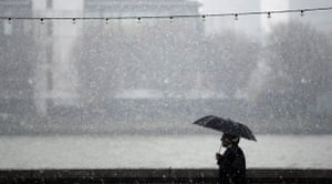 December snow: A man holds an umbrella to shelter from falling snow by the river Thames