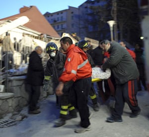 Italy earthquake: Rescue workers carry an injured woman away from her house
