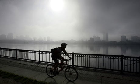 A cyclist rides along the Charles River as the fog lifts from the Boston skyline.