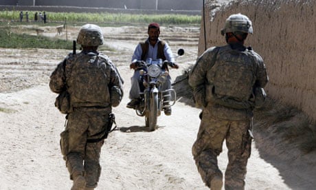 Afghan man rides his motorcycle while US soldiers search for IEDs