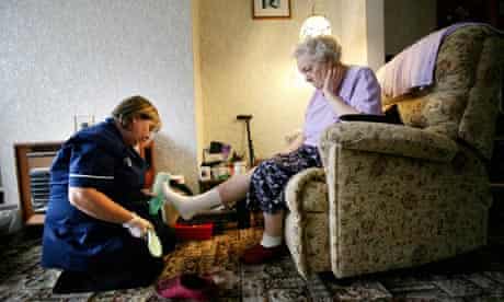 carer putting slippers on elderly woman sitting in armchair