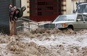 Madeira : People look on as cars are swept down the street in Funchal 