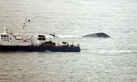 The upturned hull of the Cheonan is visible as a Korean police boat passes