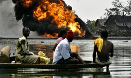 Niger Delta residents pass a burning Shell oil pipeline as they evacuate their homes by boat