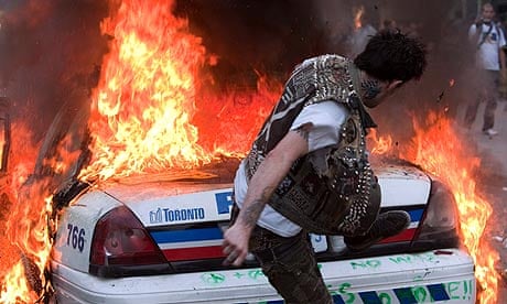 A protester kicks a burning police car in Toronto