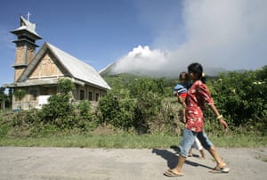 Sinabung volcano: A woman carrying her child as Mount Sinabung volcano spews smoke