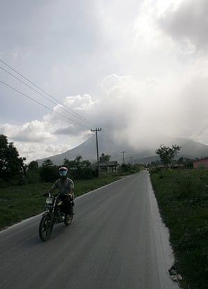 Sinabung volcano: A man rides a motorcycle as the Mount Sinabung volcano spews smoke 