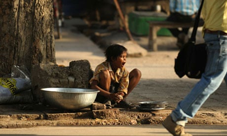 An Indian boy yawns as he washes plates