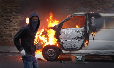 A hooded youth walks past a burning vehicle in Hackney, London, during the August riots