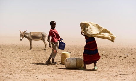 People and a donkey stand near water containers in Wajir