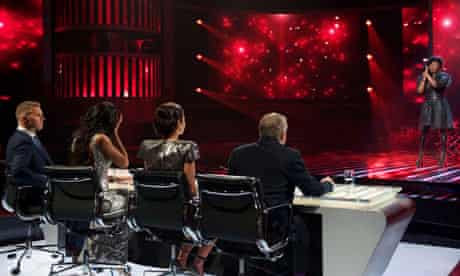 X Factor judges watch a performer on stage