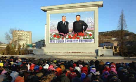 North Koreans bow in front of portraits of Kim Il-sung and Kim Jong-il 