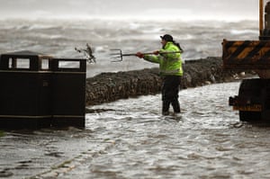 UK weather: A workman attempts to clear a drain as winds affect Helensburgh