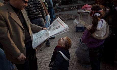 A young boy tries to read a newspaper in Cairo’s Tahrir Square