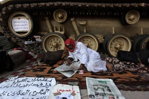 Egypt protests day 16: An Egyptian anti-government protester reads the papers near an army tank