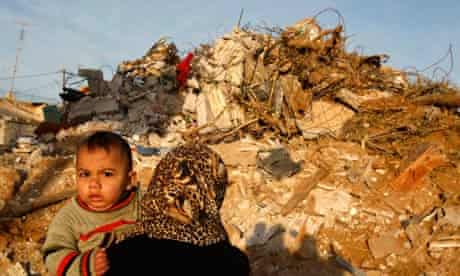 A Palestinian woman carries her child past a demolished house in the Gaza Strip