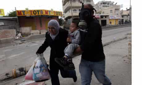 Palestinian man in gas mask helps woman and child during Nakba Day clashes 