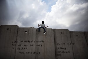 Israel violence: A masked Palestinian youth sits on top of Israel's separation barrier 
