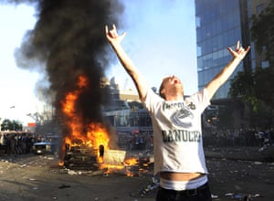 Vancouver riots: A Canucks fan yells and poses in front of a burning car as fans riot 