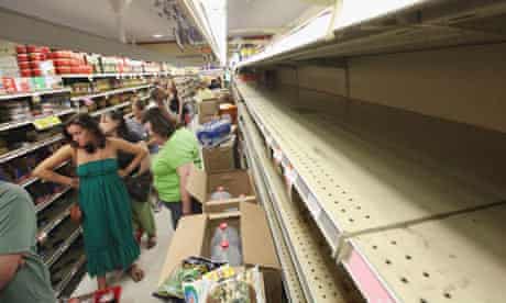 People wait in line to buy groceries next to empty shelves in a Manhattan grocery store