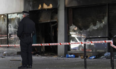A policeman stands outside damaged shops in Brixton after a second night of rioting in London