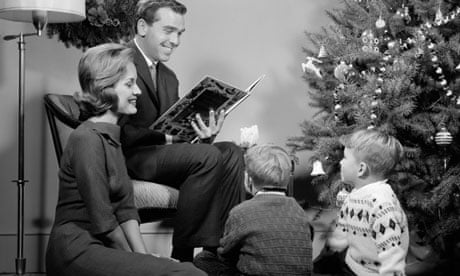 1960s Family Father Mother Two Sons Sitting By Christmas Tree In Living Room Reading A Book