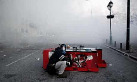 A protester wearing a gas mask shelters himself as he clashes with riot police, Athens