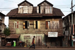 Sierra Leone Architecture: A pedestrian walks past a traditional colonial-era Board House