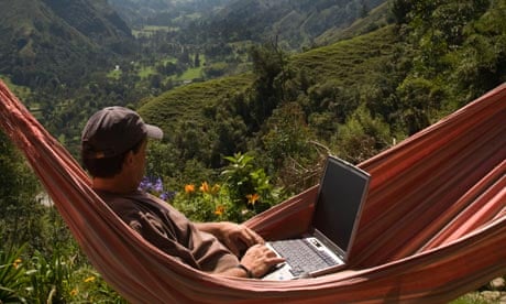 A man relaxes in a hammock whilst using his laptop