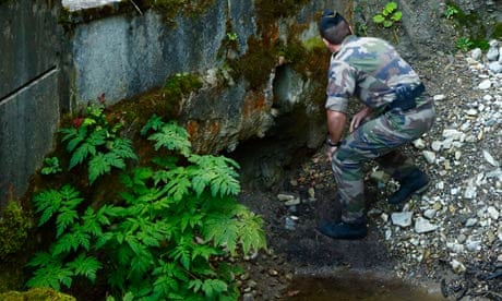 A French police officer inspects a drain near the scene of the Alps shootings