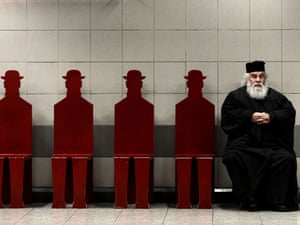 A Greek Orthodox priest sits on a bench in an Athens metro station