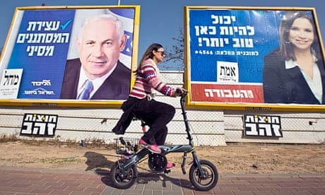 An Israeli woman rides her bicycle past election posters 