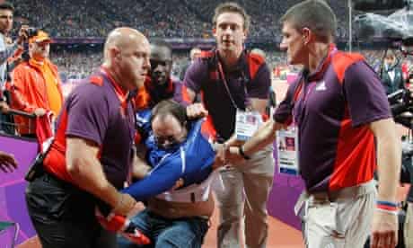 A man is detained by security shortly after an incident at the start of the men's 100m final