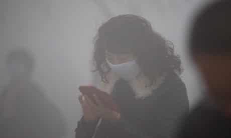 A woman wearing a mask uses her mobile phone in the smog in Harbin.