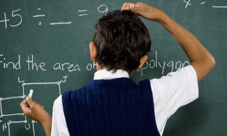 Rear view of boy at chalkboard doing math formulas and scratching head