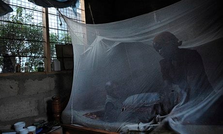 A mother and her child sit on a bed covered with a mosquito net in Bagamoyo, Tanzania