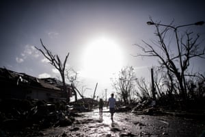 A man and a woman walk past broken trees as the sun rises on the 7th day of  the Typhoon Haiyan disaster in Tacloban, on the eastern island of Leyte.