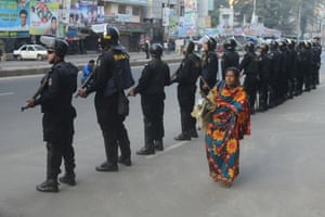 A woman walks past rapid action battalion personnel in Dhaka after Bangladesh opposition supporters went on the rampage, blocking roads and ripping up railway tracks after rejecting plans for an election in January.
