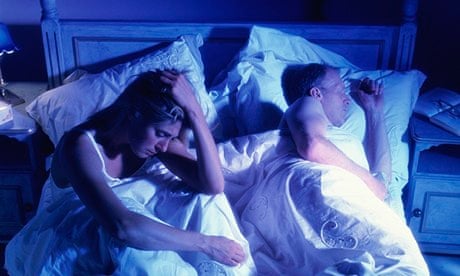 A sleepless woman in bed beside a sleeping man